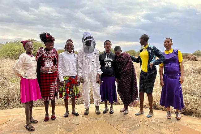 The Maasai women gathered and one in a beekeeping suit